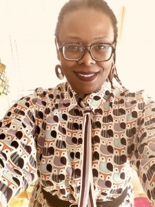 selfie of black woman with square glasses, hair pulled back and wearing an owl-print dress